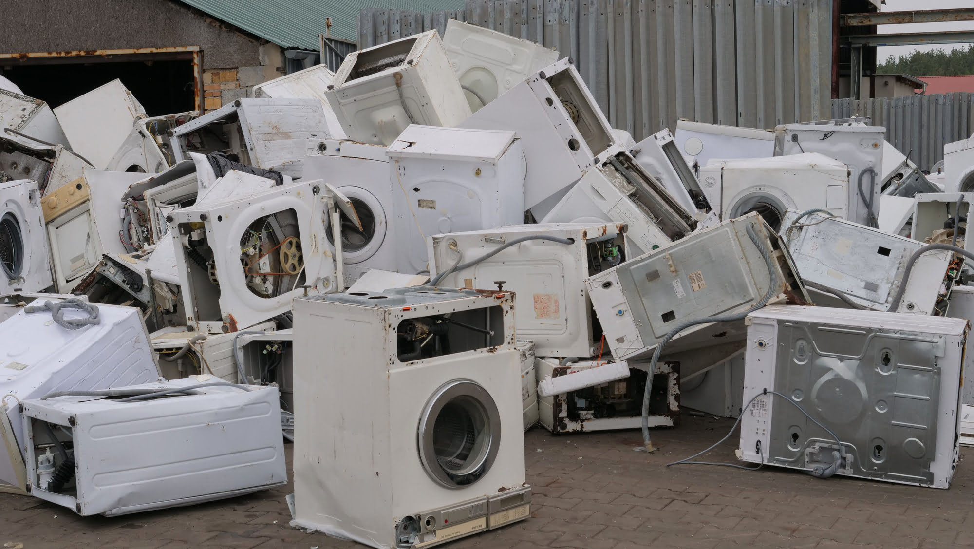 pile of broken washing machines and dryers at a scrapyard